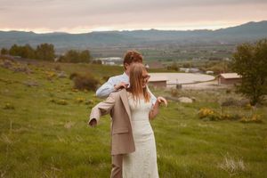 A couple embraces on a hilltop overlooking a scenic valley landscape at sunset with mountains in the distance.