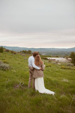 Couple enjoying a romantic moment on a grassy hillside overlooking mountains at sunset.