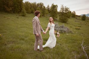 A couple in wedding attire holds hands in a green meadow on their special day.
