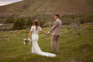 A couple stands together in a scenic mountain meadow during their wedding celebration with rolling hills in the background.