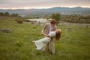 Couple embracing on blanket in field with mountain landscape and sunset in background.