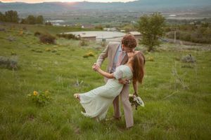 Couple in a romantic meadow embrace with mountains in the background during golden hour.