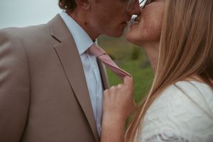 Close up romantic moment showing hands tugging on pink tie with blurred faces in soft focus.