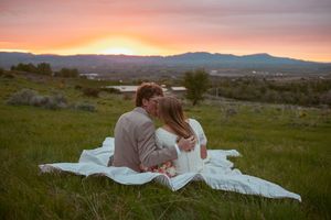 Wedding couple embraces on a blanket during sunset with mountains in the background.