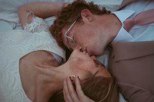Couple sharing an intimate moment while lying together on soft white bedding and linens.