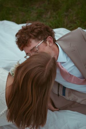 A couple embraces and shares a tender kiss while lying on white bedding.