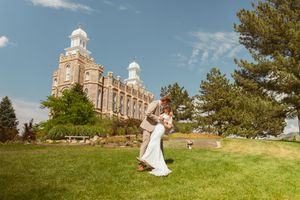 A scenic wedding photo shoot on a hilltop with a grand historic building and blue sky in the background.