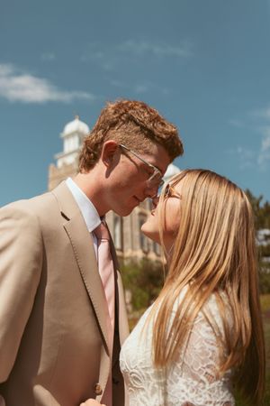 A romantic wedding couple sharing an intimate moment against a blue sky with a historic building in the background.