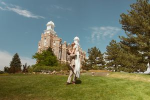 A historic stone castle or fortress sits atop a grassy hill under blue skies with scattered clouds.