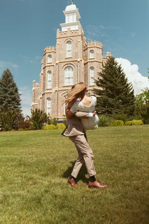 A joyful embrace in front of a grand historic brick temple with white spires against a blue summer sky.