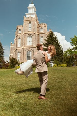 Candid sequence of a couple doing cartwheels on a grassy hill with a historic brick church building in the background.