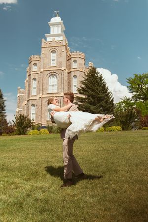 A romantic dance sequence shows a couple performing a dramatic dip move on a hillside with a stone church behind them.