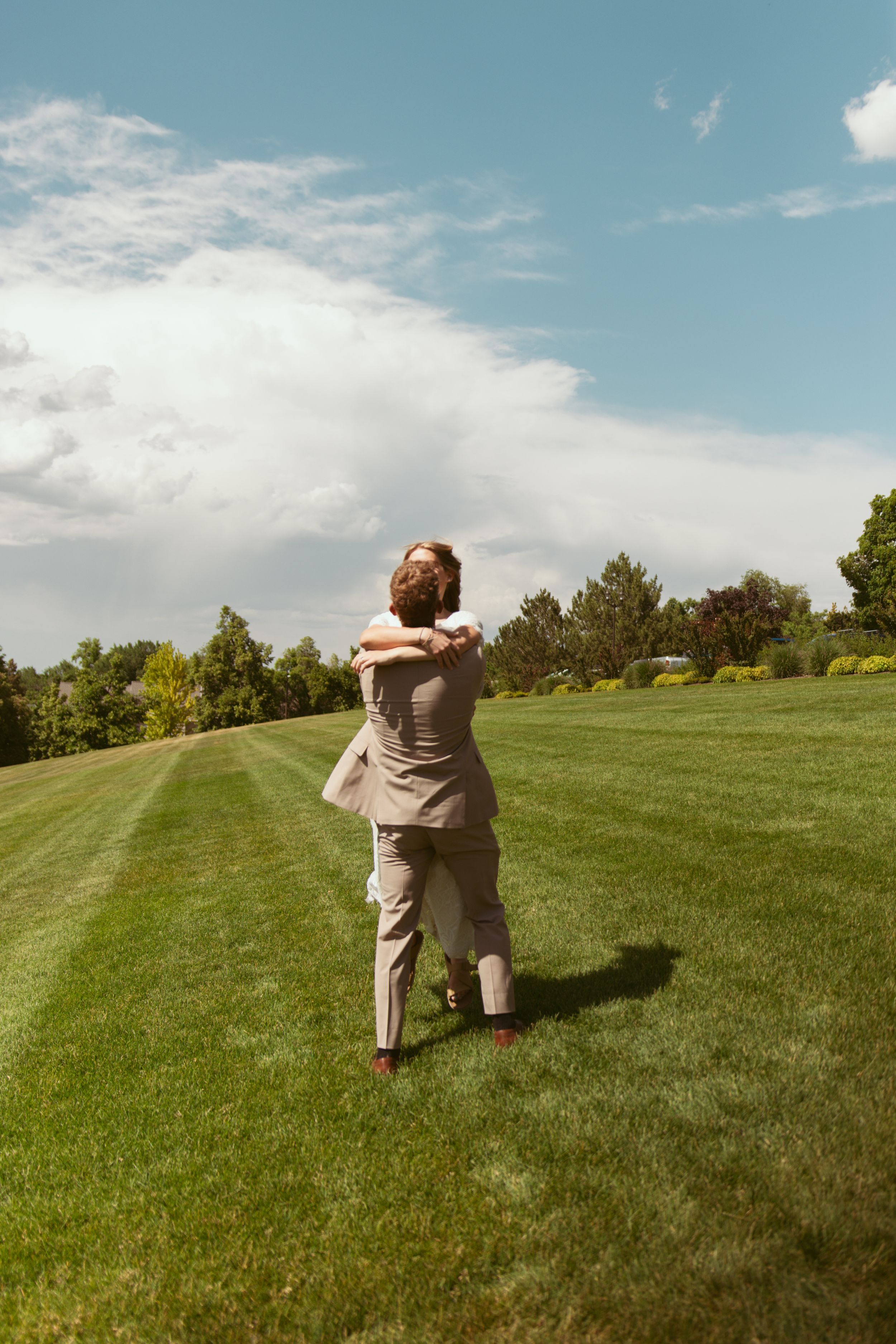 A romantic embrace captured on a sunny day with rolling green hills and trees in the background.