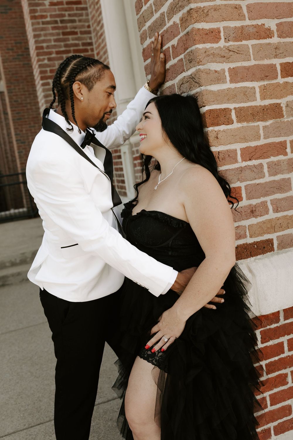 A couple shares playful dance moves against a brick wall backdrop.