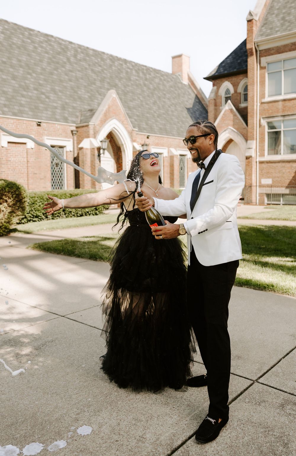 A couple dances playfully outdoors, one wearing a flowing black dress and the other in a white jacket.