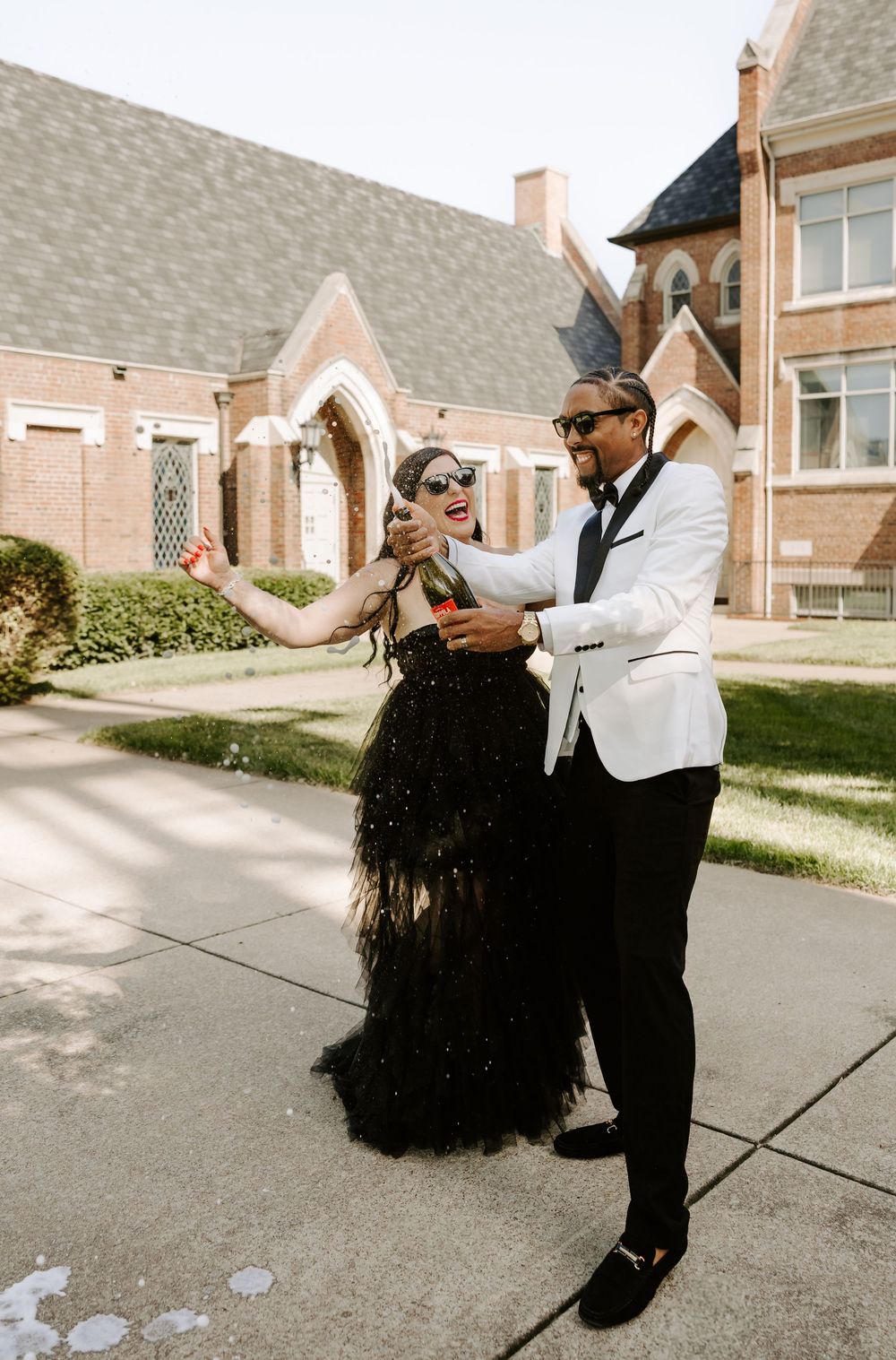 A couple performs a dramatic dance dip on a driveway with residential buildings in the background.