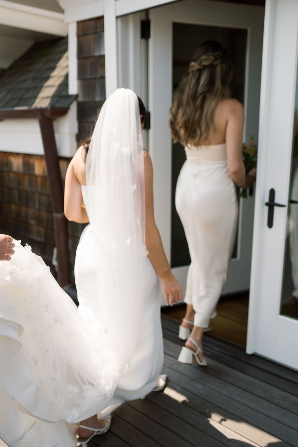 Multiple silhouettes of a bride walking along a white porch in sunlight.