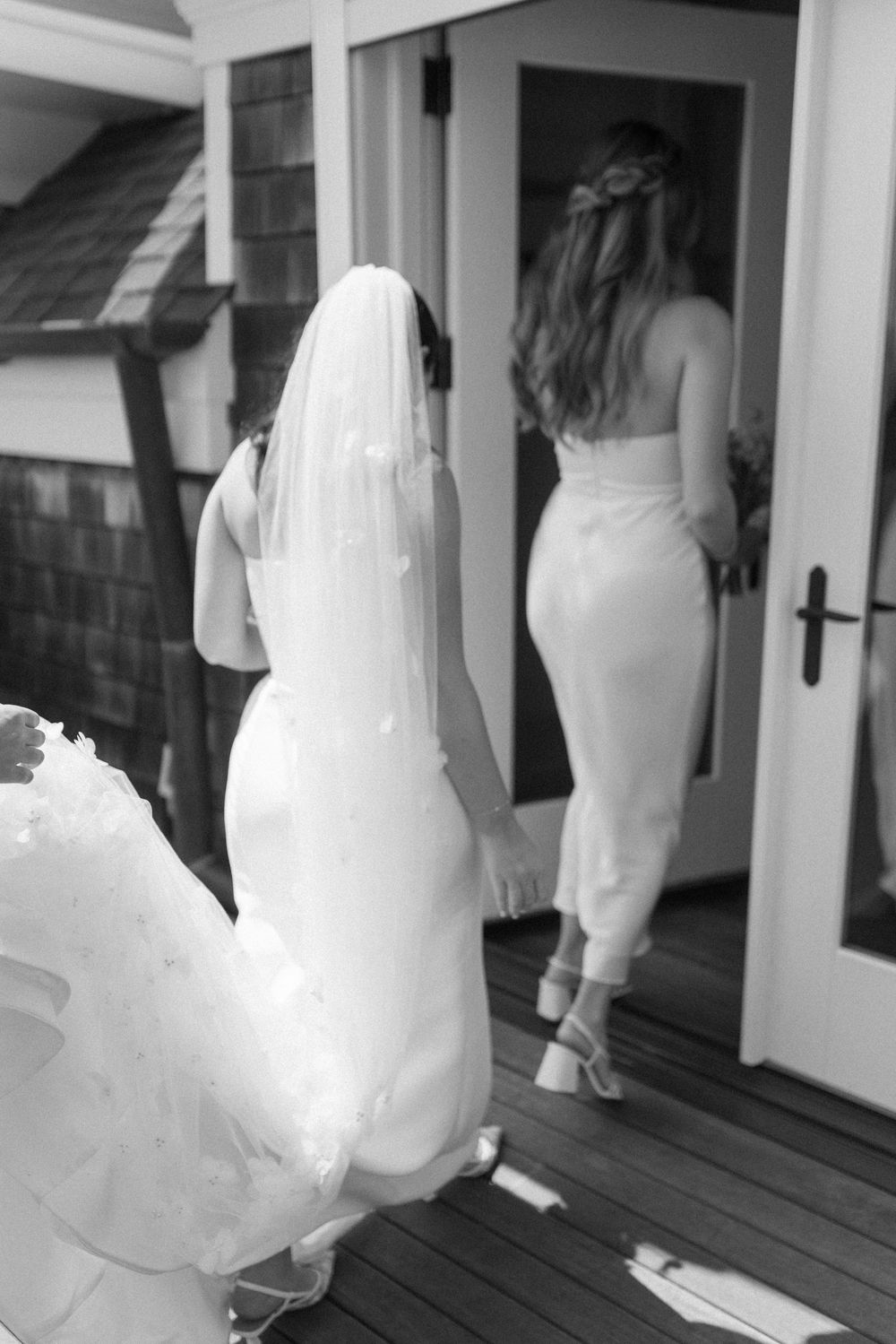 A silhouette of a bride in a flowing dress walks along a white porch.