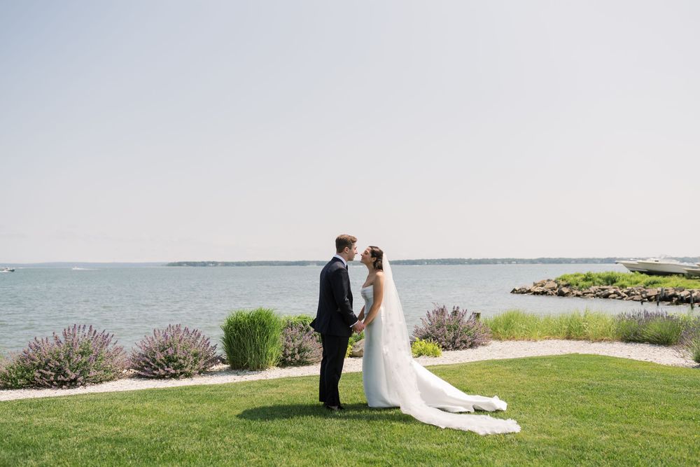 Wedding couple stands together on manicured lawn overlooking the ocean.