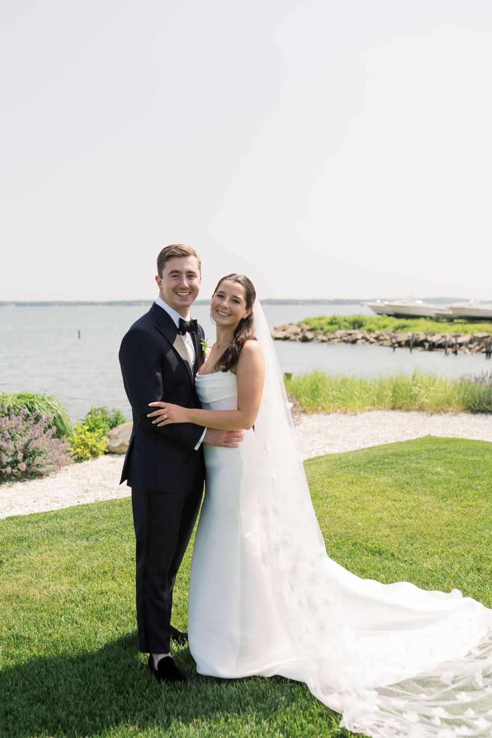 Happy couple poses for wedding portraits on a coastal lawn with ocean views.