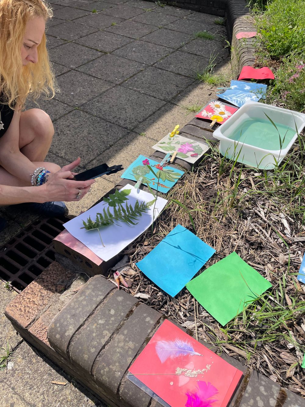 Colorful artwork and paintings laid out on a sidewalk with vibrant paper sheets displaying various artistic creations.
