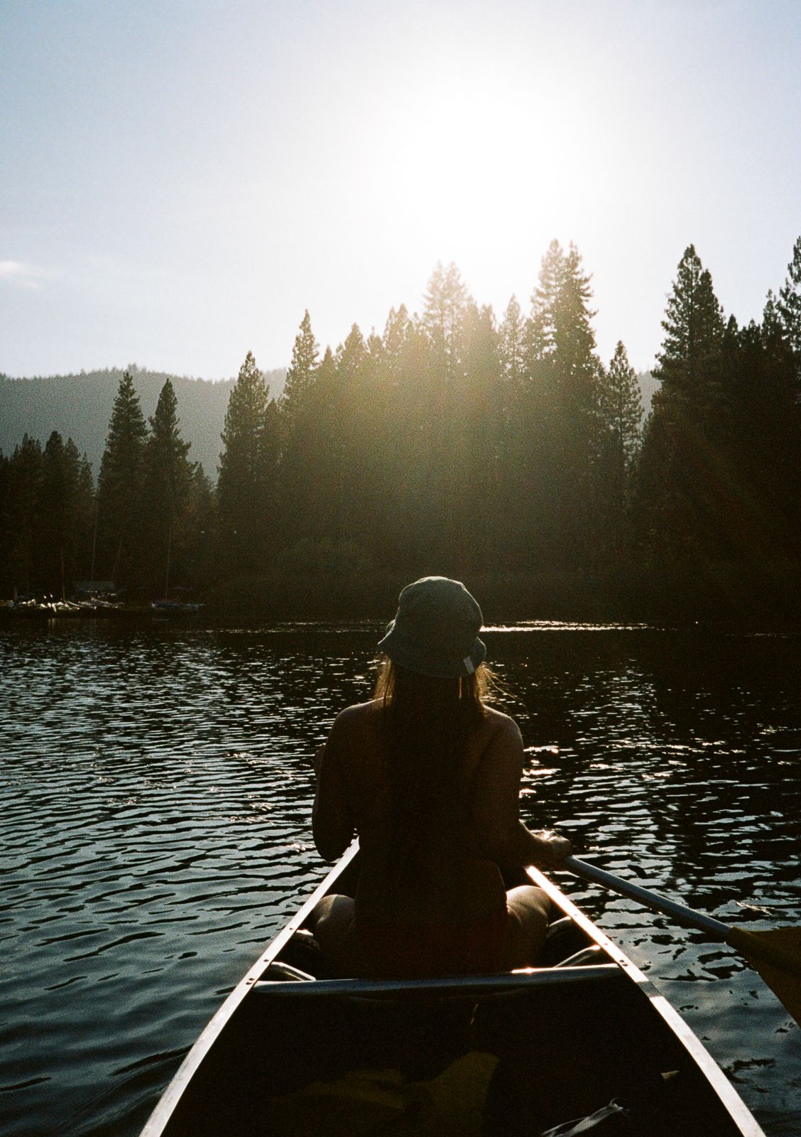 Silhouette of person in canoe at sunset with forest skyline.
