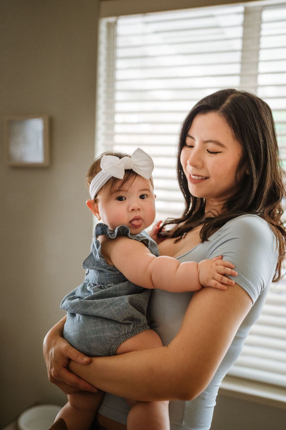 A tender moment between parent and baby wearing grey in front of sunlit windows.