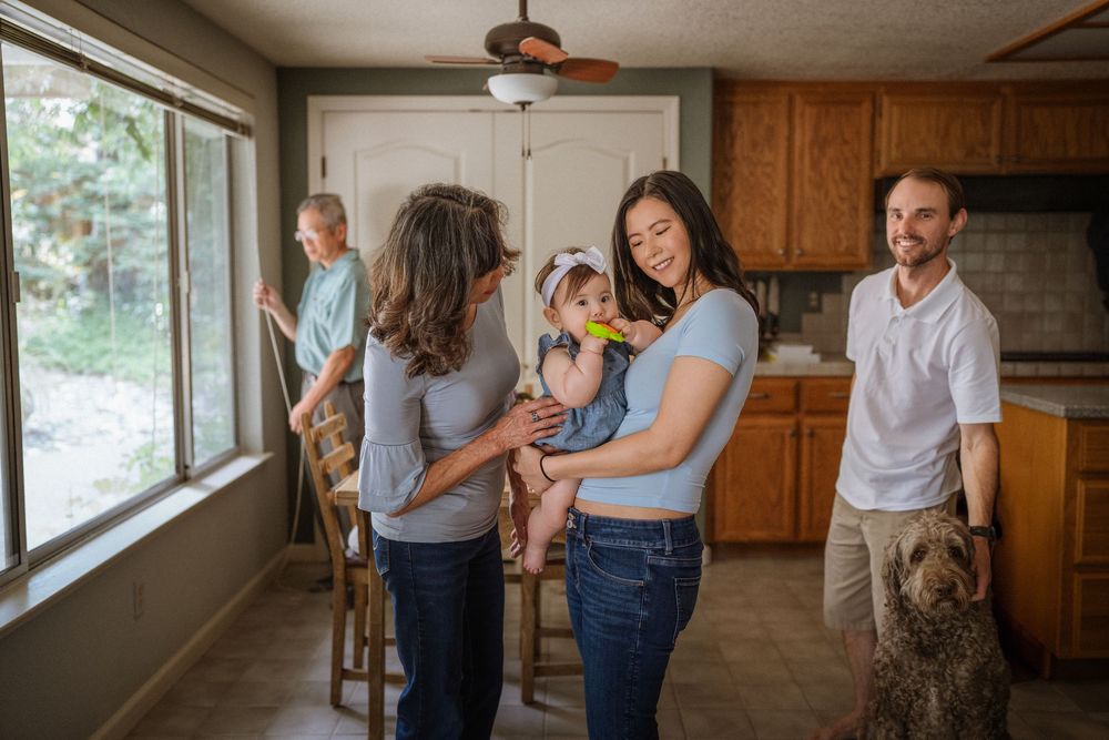 Natural light streams through windows as family members interact in their kitchen space.