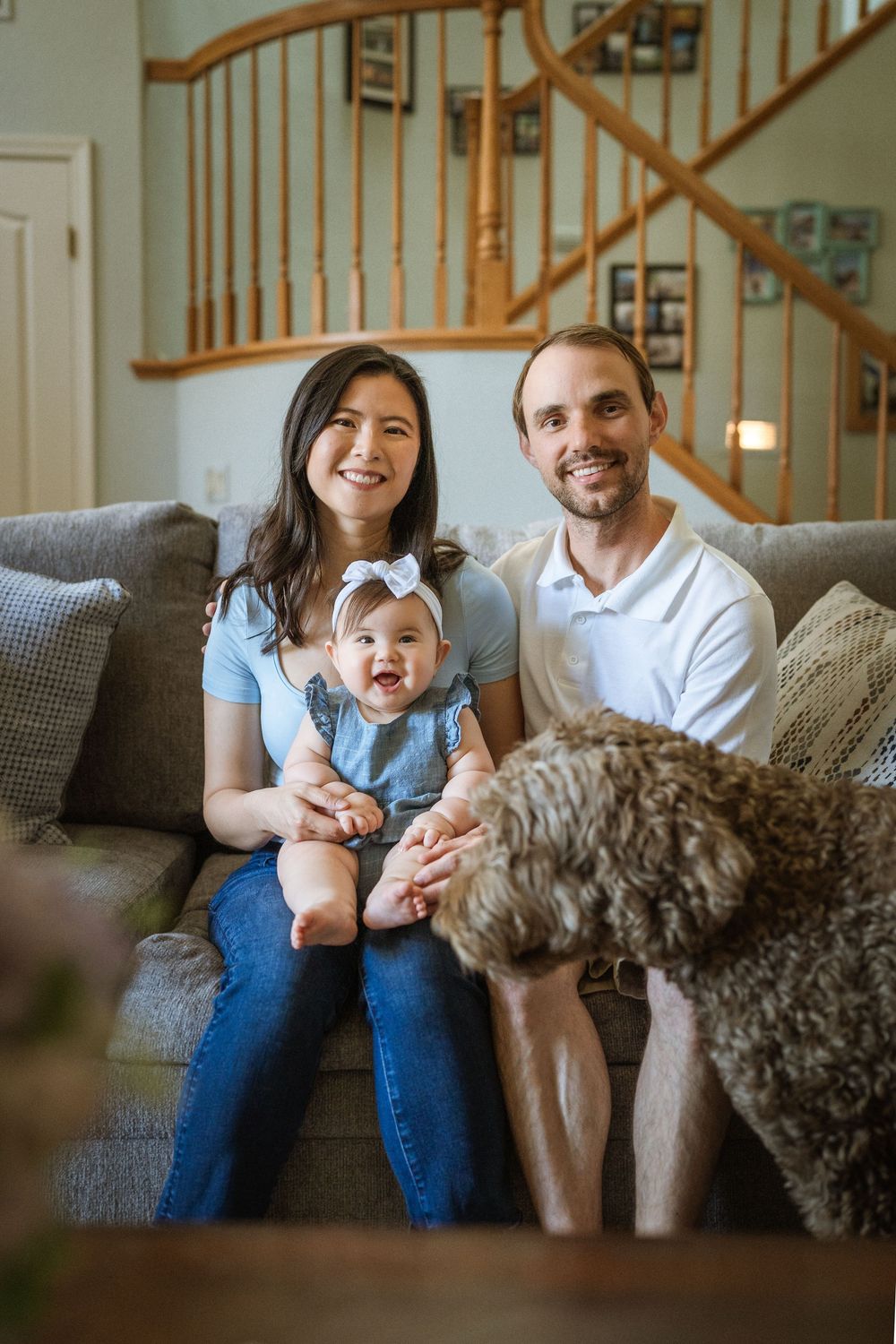 A relaxed family moment on a grey couch with their fluffy doodle dog nearby.