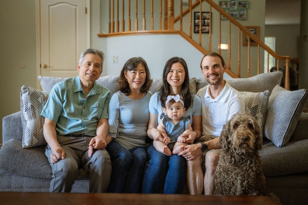 Family portrait on grey couch with their curly-haired doodle dog in a living room setting.