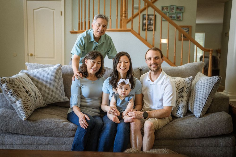 A family relaxes together on a light grey couch in their living room.