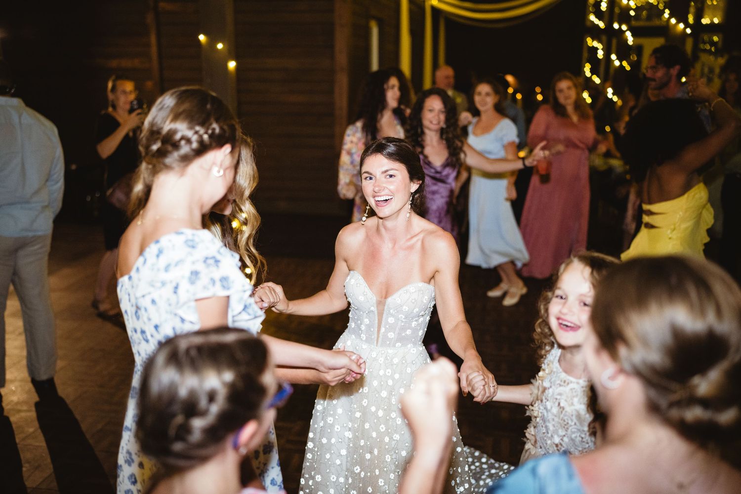 Wedding guests dancing together during an energetic reception celebration with glowing lights in the background.