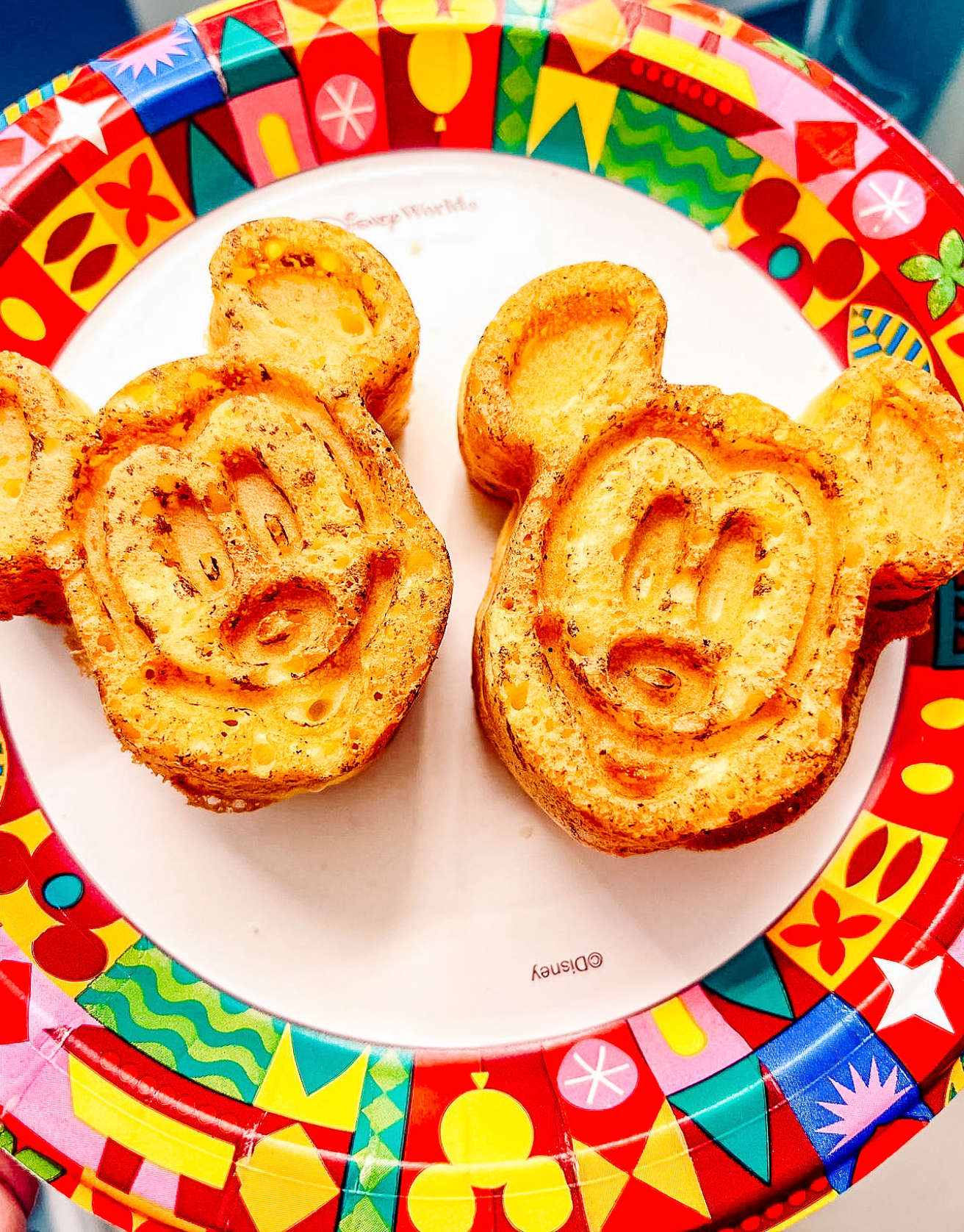 Mickey Mouse-shaped pastries on a decorative Disney plate with colorful festive border pattern.