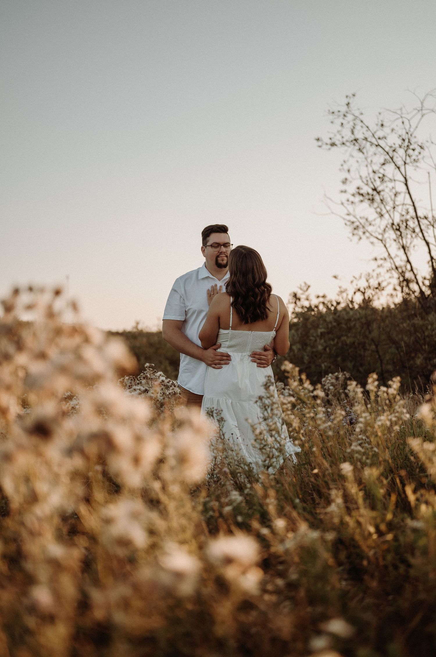 Couple embracing on beach at sunset with lake and clouds in background.