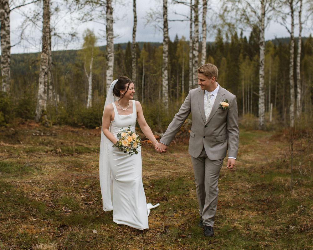 Ett brudpar som går hand i hand i en björkskog.