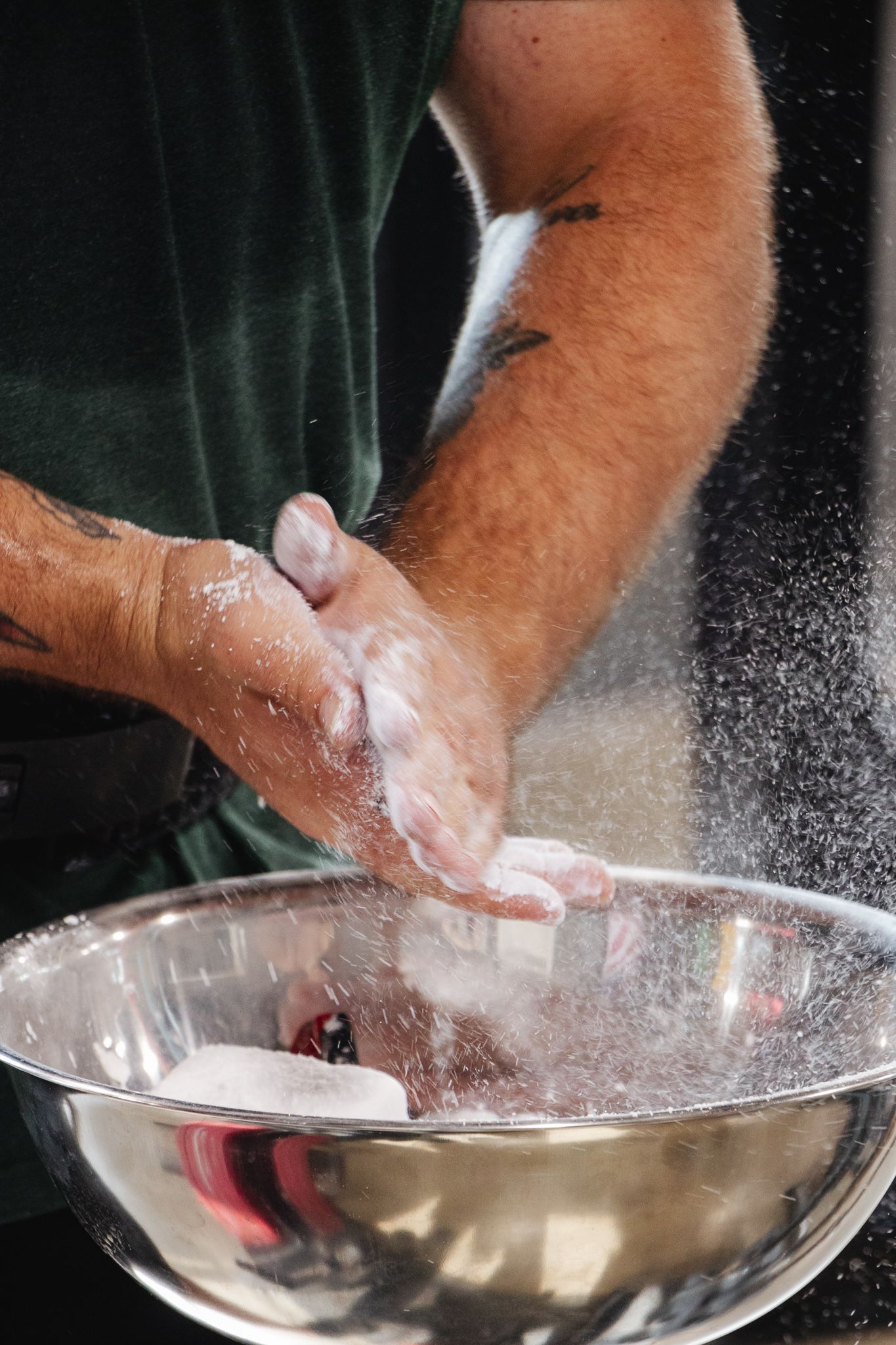 Man claps chalked hands over a metal bowl, sending a cloud of chalk dust into the air before lifting weights