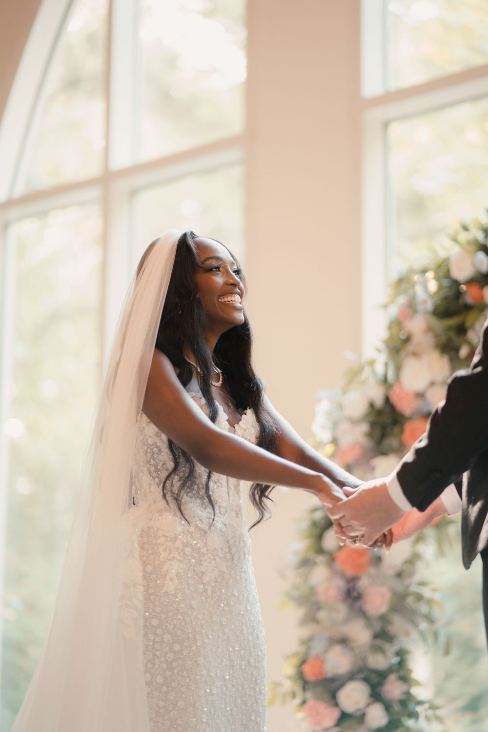 A joyful bride in a white beaded dress laughs and dances during an intimate indoor wedding ceremony.