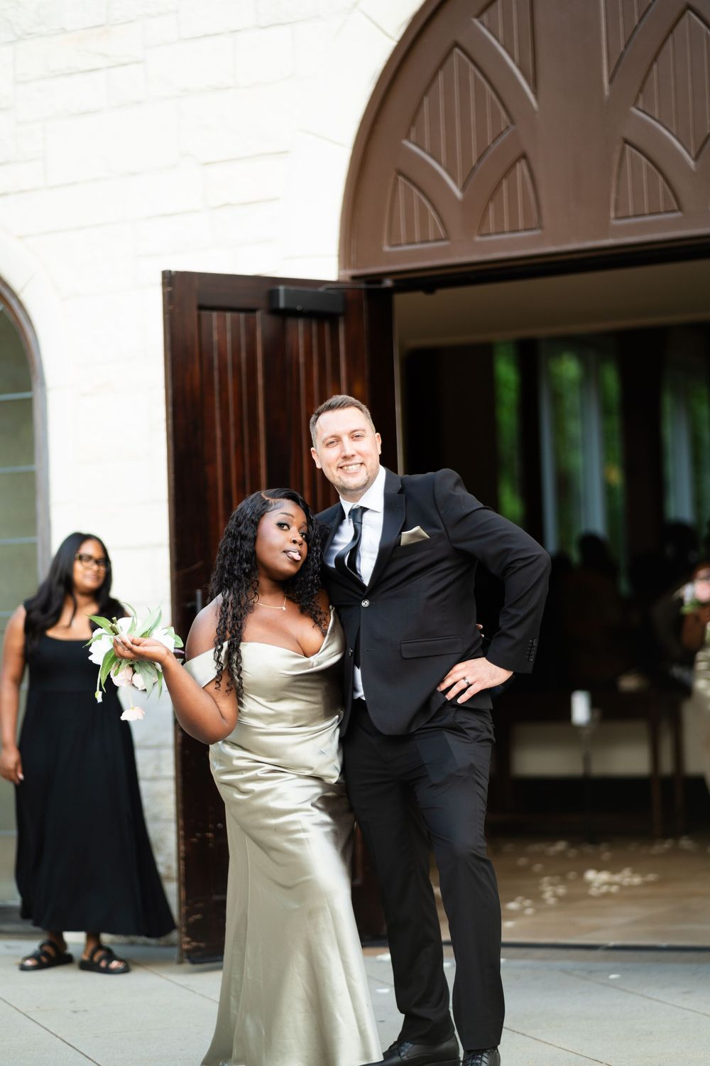 A bride and groom share a joyful candid moment together outdoors near large wooden doors at their wedding.