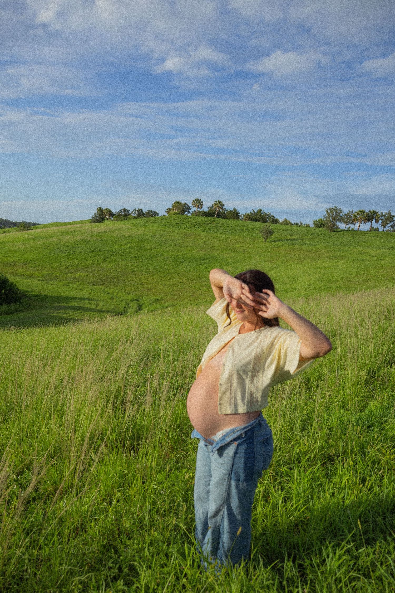 Figure standing in a meadow of tall grass under a vibrant blue sky with white puffy clouds on a sunny day.