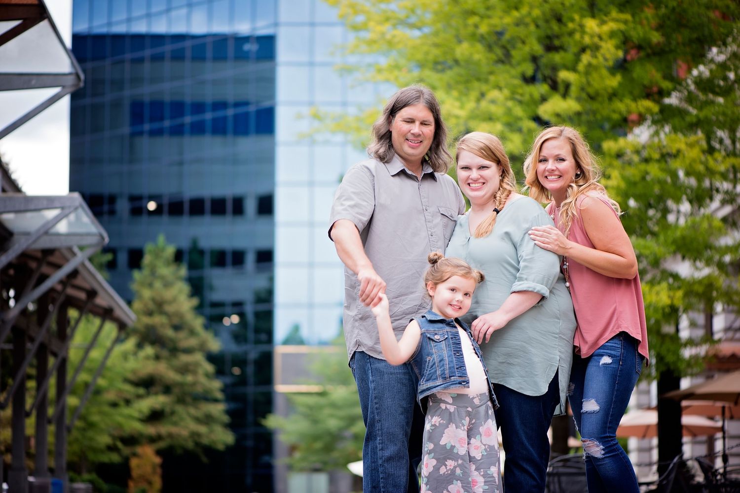 A family group cheerfully poses together outdoors near modern office buildings and trees.