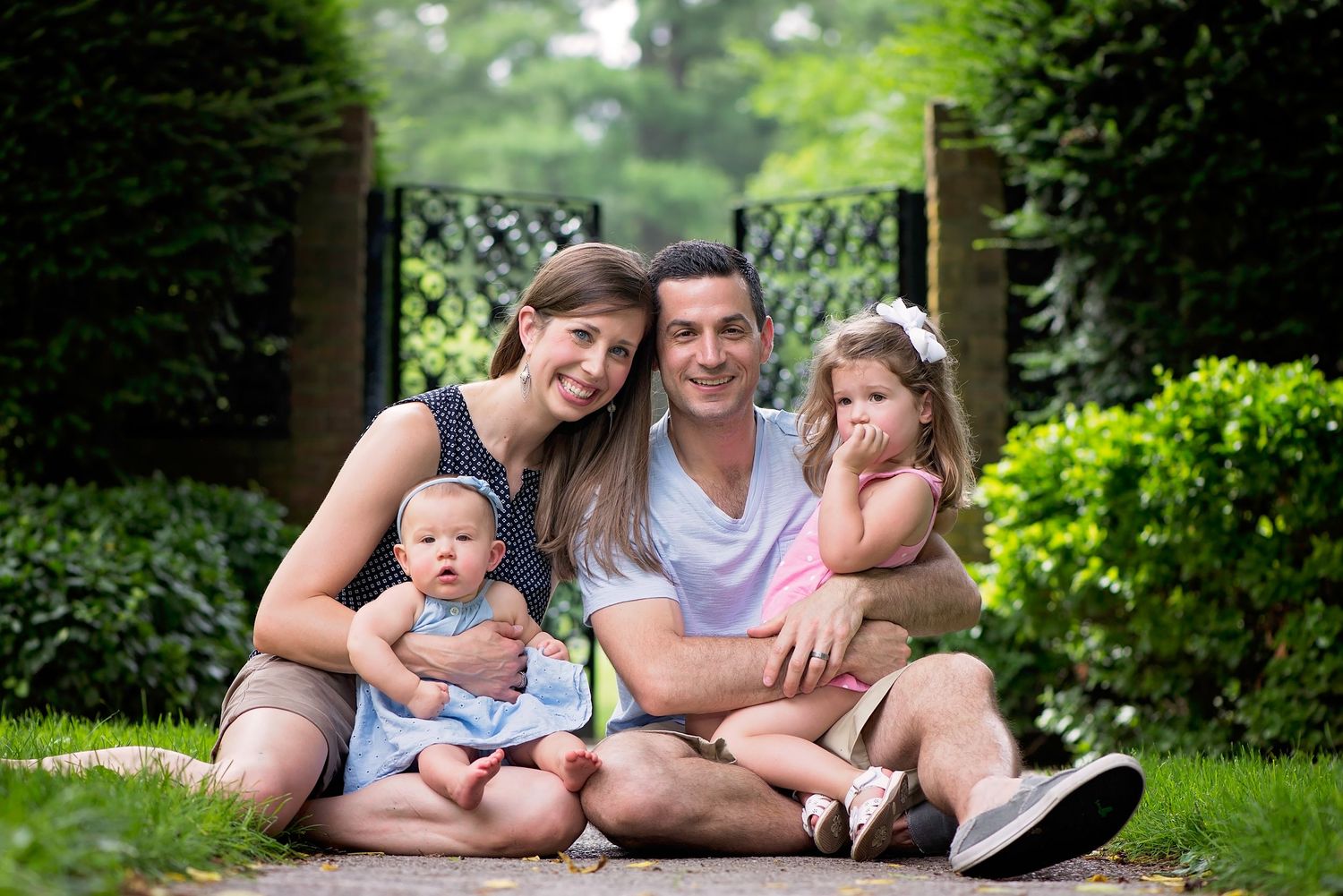 Young family relaxing together on a garden path surrounded by lush greenery on a summer day.