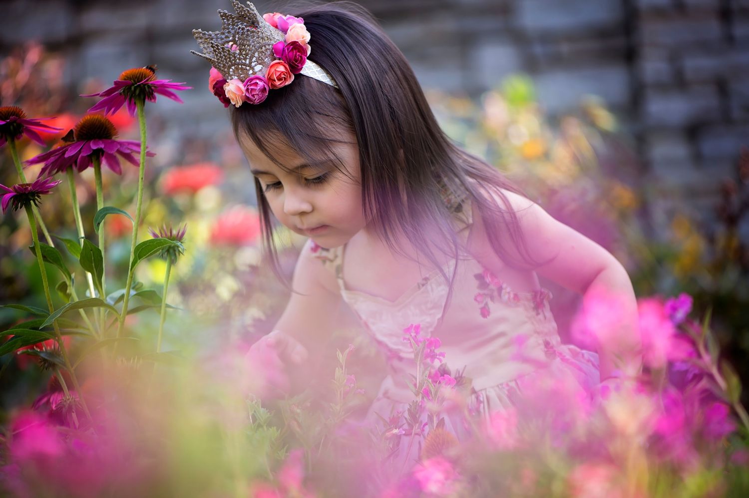 Someone in a pink dress admires vibrant pink and purple flowers in a summer garden.