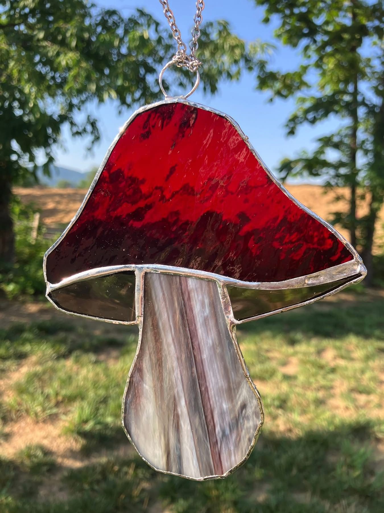 A handcrafted stained glass mushroom sun catcher featuring a rich red cap and textured neutral toned stem