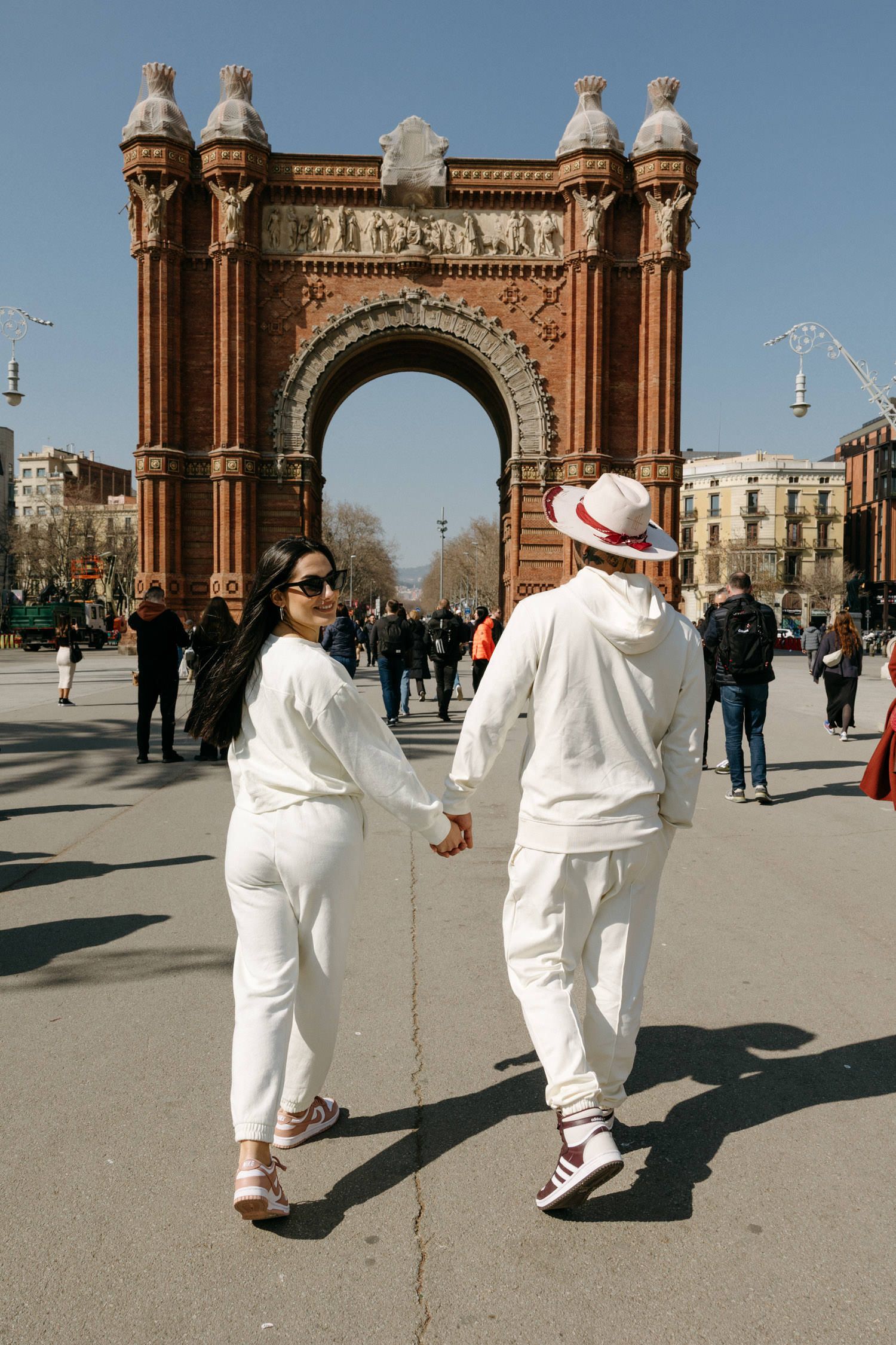 Two people in white outfits walking near the Arc de Triomf in Barcelona.