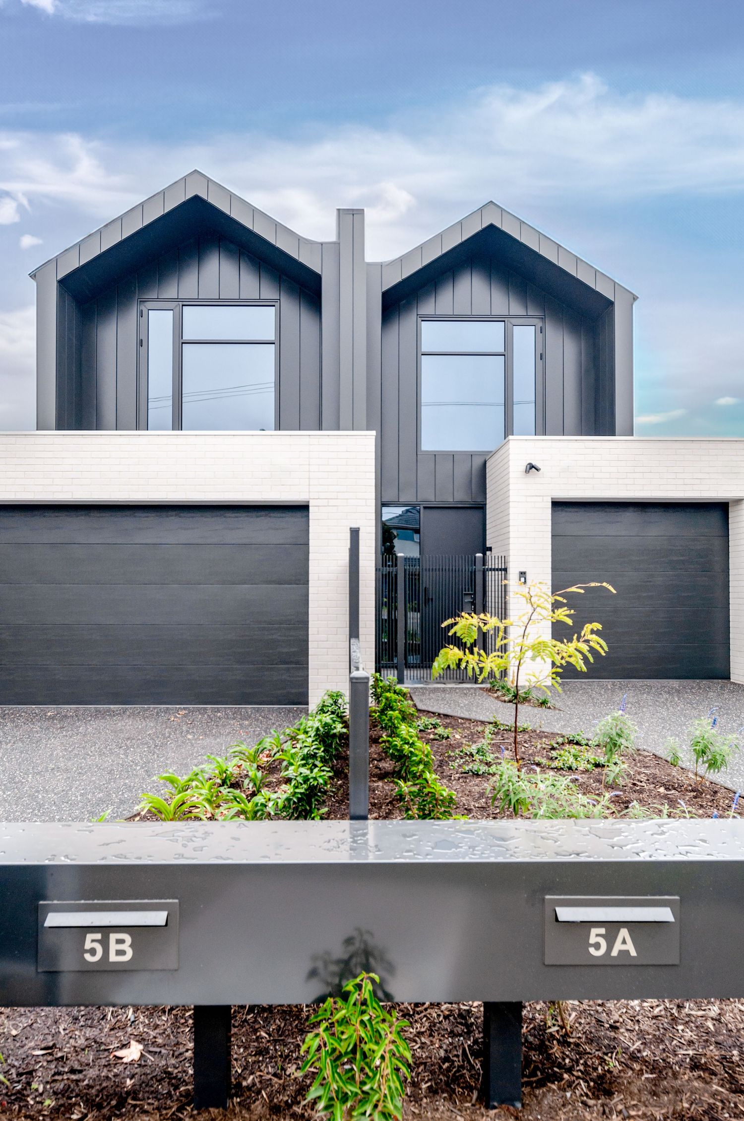Modern duplex townhouse with gray exterior, matching garage doors, and black mailboxes numbered 5A and 5B.