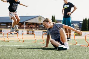 Athletes train on a turf field with agility hurdles while stretching and warming up during outdoor practice.