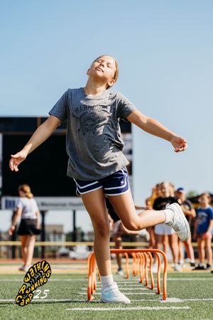 Student athlete practices agility drills by jumping over orange hurdles on outdoor field during sports training session.