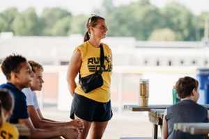 Athletes gather along a waterfront during an outdoor training session, wearing yellow and blue team uniforms.