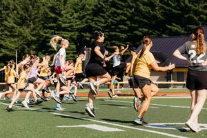 Athletes perform synchronized exercises on an outdoor sports field during summer training camp.