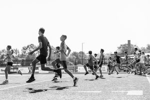 A group of people jump in unison on an outdoor track during a black and white athletic activity.